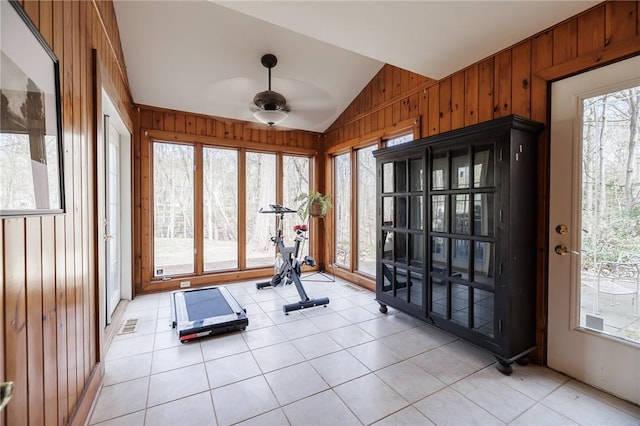 exercise area with wooden walls, a ceiling fan, vaulted ceiling, and a healthy amount of sunlight