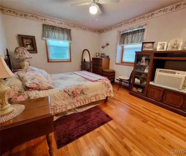 bedroom featuring a ceiling fan, a wall unit AC, and wood finished floors