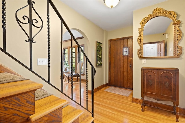 foyer with stairs, arched walkways, baseboards, and light wood finished floors