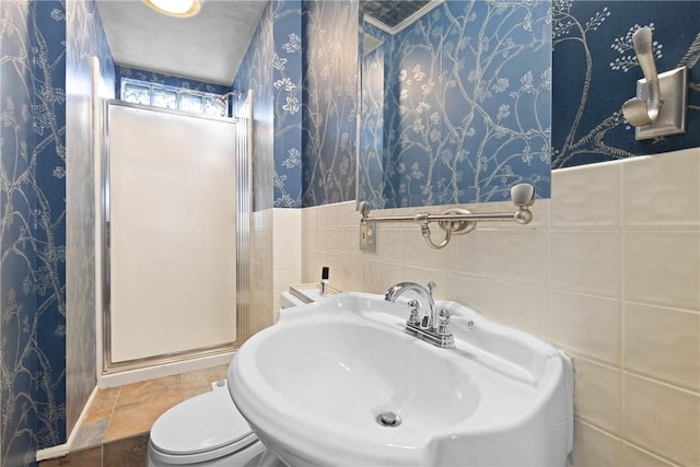 bathroom with a sink, a shower stall, toilet, and wallpapered walls