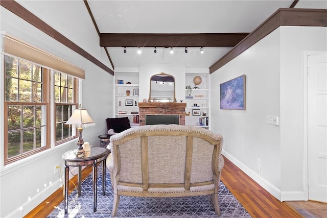 living area featuring a brick fireplace, built in shelves, wood finished floors, baseboards, and beamed ceiling