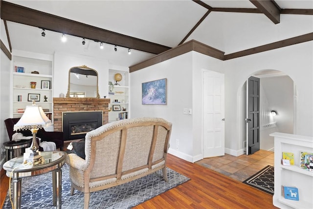 living area featuring arched walkways, a fireplace, built in shelves, wood finished floors, and baseboards
