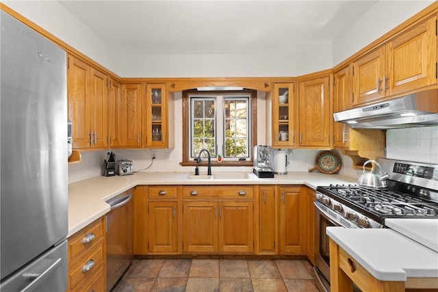 kitchen with brown cabinetry, a sink, under cabinet range hood, and stainless steel appliances