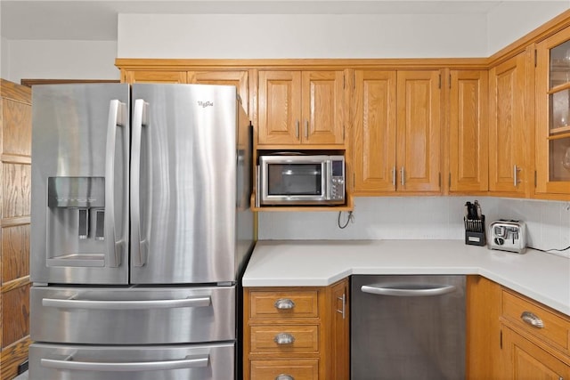 kitchen with light countertops, appliances with stainless steel finishes, glass insert cabinets, and tasteful backsplash