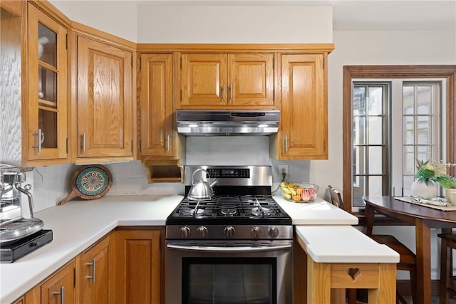 kitchen with decorative backsplash, glass insert cabinets, stainless steel gas range oven, light countertops, and ventilation hood