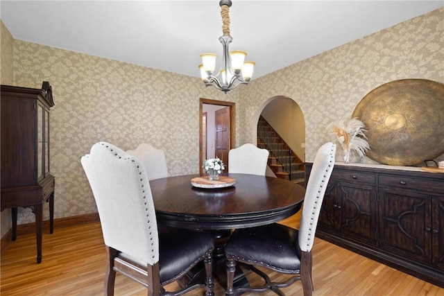 dining space featuring light wood-style floors, arched walkways, wallpapered walls, and a chandelier