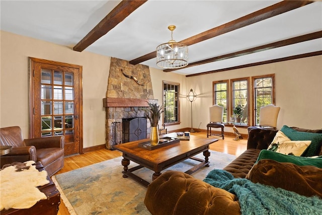 living area featuring wood finished floors, beamed ceiling, a stone fireplace, baseboards, and a chandelier