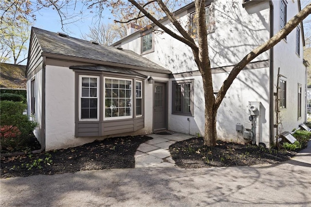 exterior space with roof with shingles, stucco siding, and a chimney