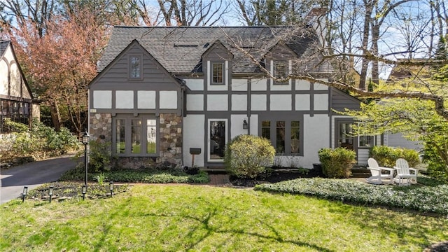 tudor home with a front yard, a shingled roof, stone siding, and stucco siding