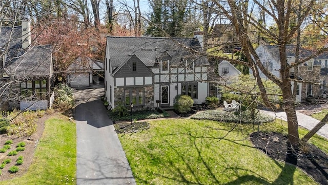 tudor home with a shingled roof, stucco siding, and a front yard