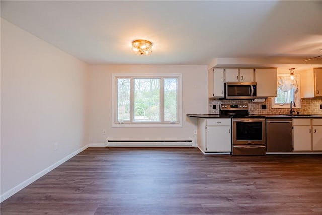 kitchen with dark countertops, a sink, baseboard heating, stainless steel appliances, and tasteful backsplash