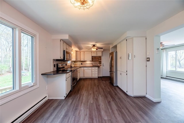 kitchen with stainless steel appliances, dark countertops, a baseboard heating unit, and dark wood-style floors
