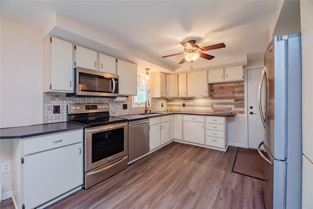 kitchen featuring ceiling fan, appliances with stainless steel finishes, dark countertops, wood finished floors, and a sink