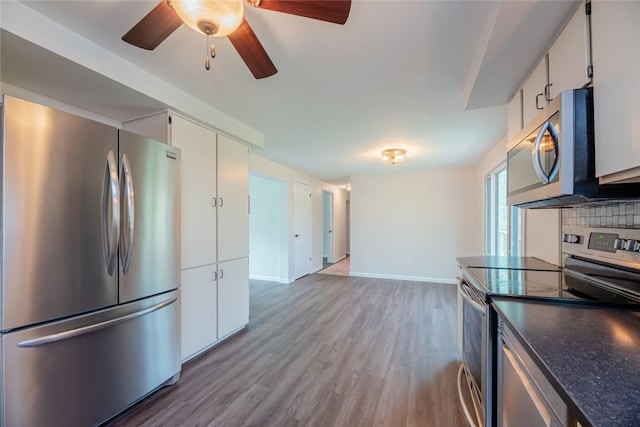 kitchen featuring ceiling fan, dark countertops, wood finished floors, baseboards, and stainless steel appliances