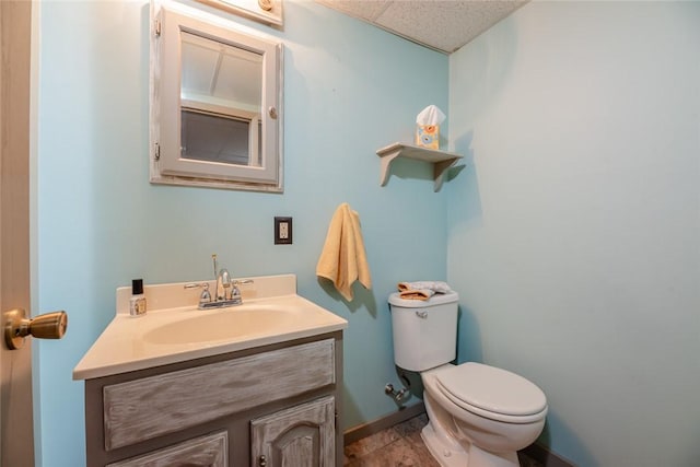 bathroom featuring vanity, baseboards, a drop ceiling, and toilet