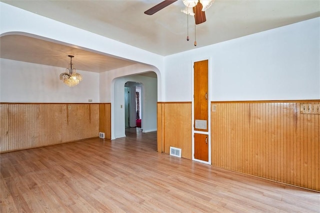 spare room with arched walkways, visible vents, wainscoting, and wood finished floors