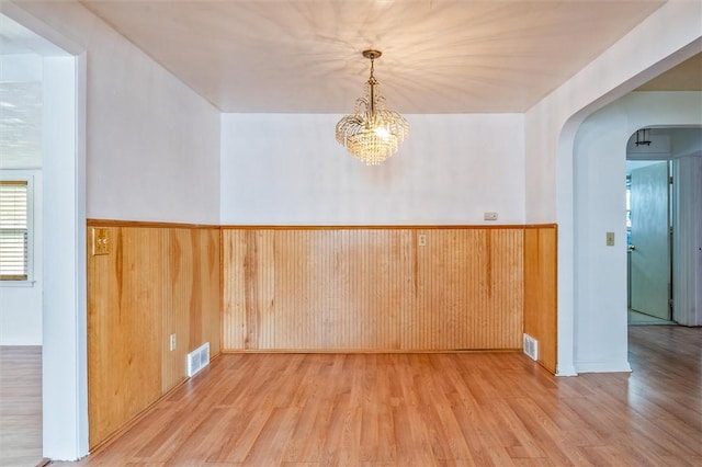 spare room with visible vents, wainscoting, wood finished floors, wooden walls, and arched walkways