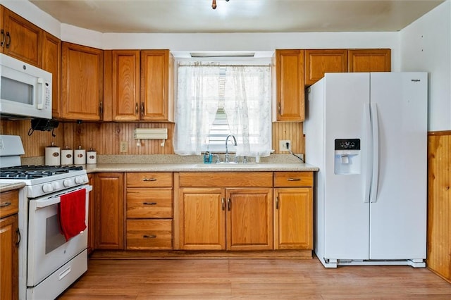 kitchen with brown cabinetry, a sink, white appliances, and light countertops