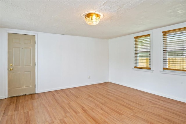 empty room with light wood-style floors, baseboards, and a textured ceiling