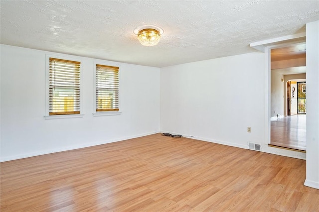 spare room featuring a textured ceiling, visible vents, baseboards, and light wood-style floors