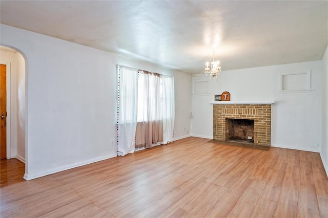 unfurnished living room featuring an inviting chandelier, arched walkways, light wood finished floors, and a brick fireplace
