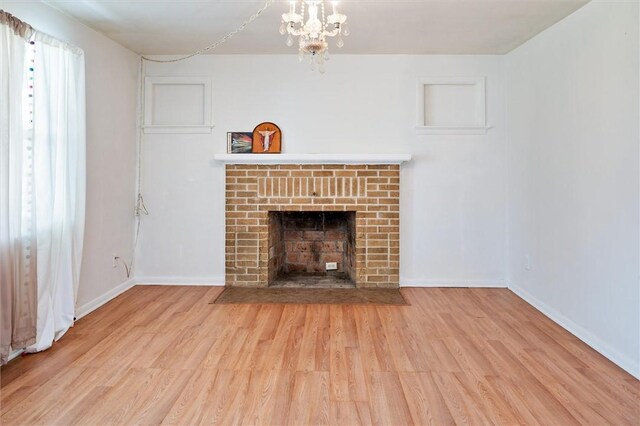 unfurnished living room with baseboards, wood finished floors, a notable chandelier, and a fireplace