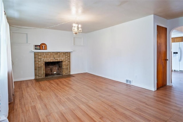 unfurnished living room featuring visible vents, a fireplace, a chandelier, arched walkways, and light wood finished floors