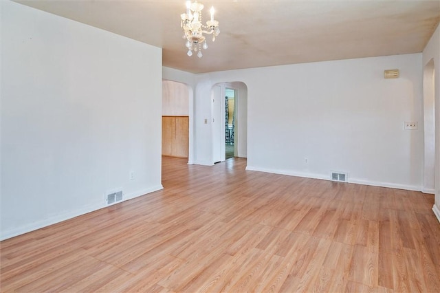 spare room with arched walkways, a notable chandelier, light wood-type flooring, and visible vents