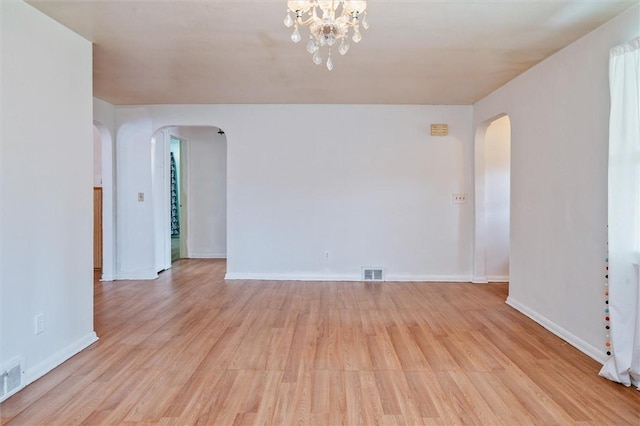 spare room featuring arched walkways, baseboards, visible vents, and light wood finished floors
