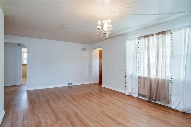 unfurnished room featuring visible vents, arched walkways, baseboards, an inviting chandelier, and light wood-style flooring