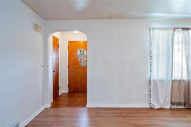 spare room featuring arched walkways, baseboards, wood finished floors, and visible vents