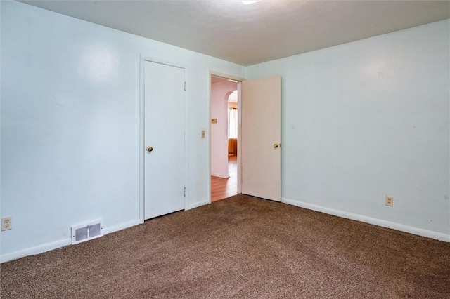 unfurnished room with arched walkways, baseboards, visible vents, and dark carpet