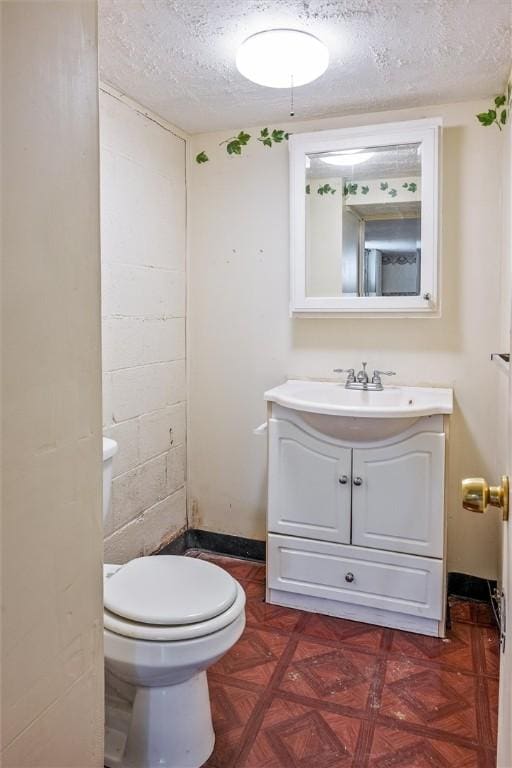 bathroom with vanity, concrete block wall, a textured ceiling, and toilet