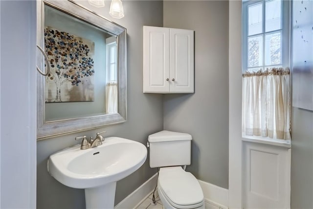 half bath with baseboards, a sink, and toilet