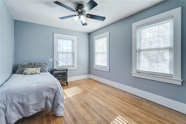 bedroom with a ceiling fan, baseboards, multiple windows, and light wood-style flooring