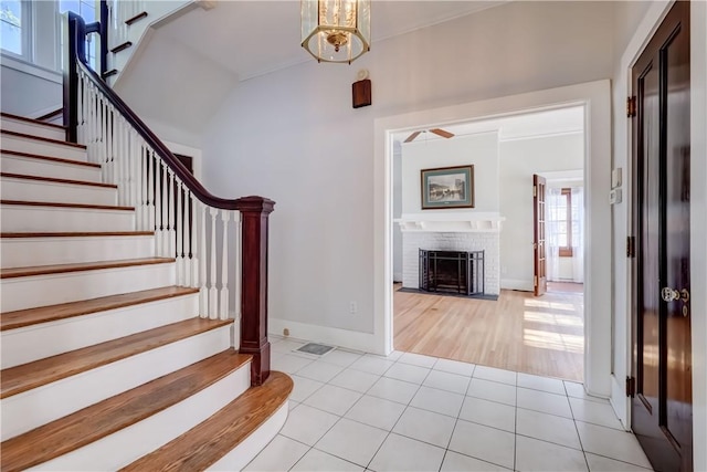 foyer featuring a brick fireplace, baseboards, stairway, a chandelier, and light tile patterned floors