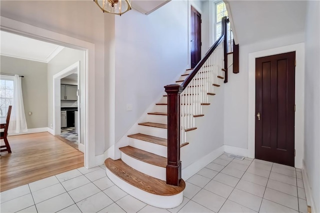 foyer entrance with crown molding, baseboards, stairs, and light tile patterned flooring