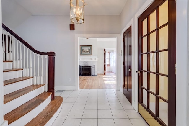 foyer entrance featuring light tile patterned floors, stairway, a fireplace, and a notable chandelier