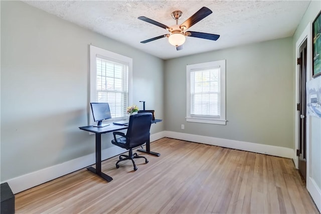 office area featuring light wood-style floors, baseboards, a ceiling fan, and a textured ceiling