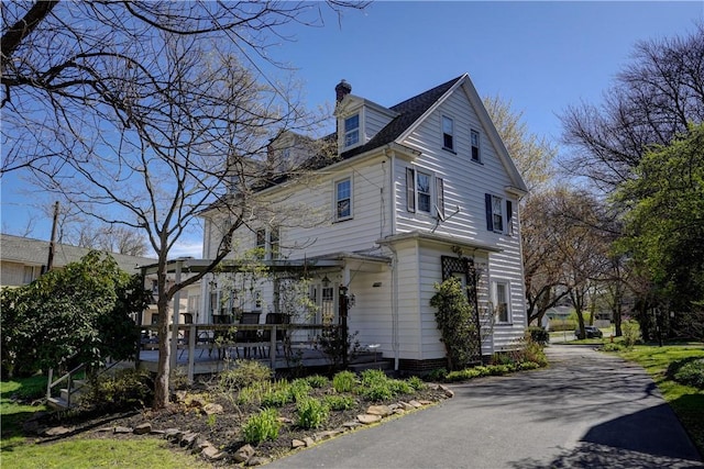 view of side of home featuring a wooden deck, a chimney, and driveway