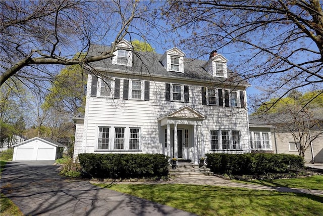 colonial home featuring a garage, a front lawn, an outbuilding, and a chimney