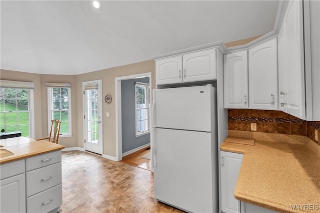kitchen featuring freestanding refrigerator, lofted ceiling, baseboards, light countertops, and white cabinetry