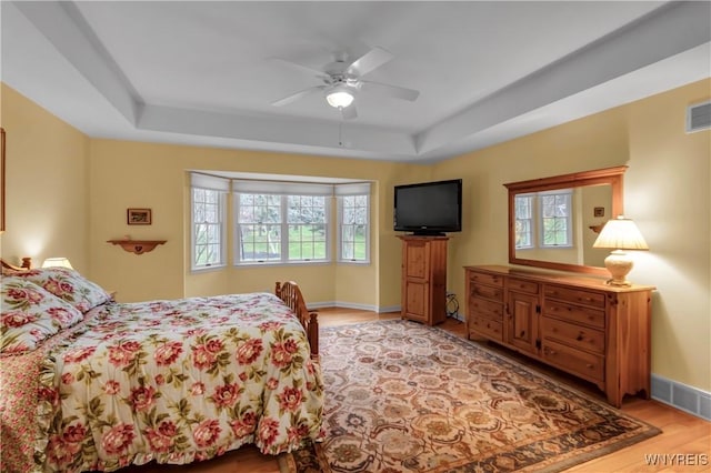 bedroom featuring visible vents, light wood-style floors, baseboards, ceiling fan, and a tray ceiling