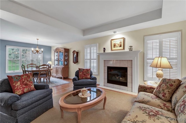 living room featuring baseboards, wood finished floors, a notable chandelier, and a tile fireplace
