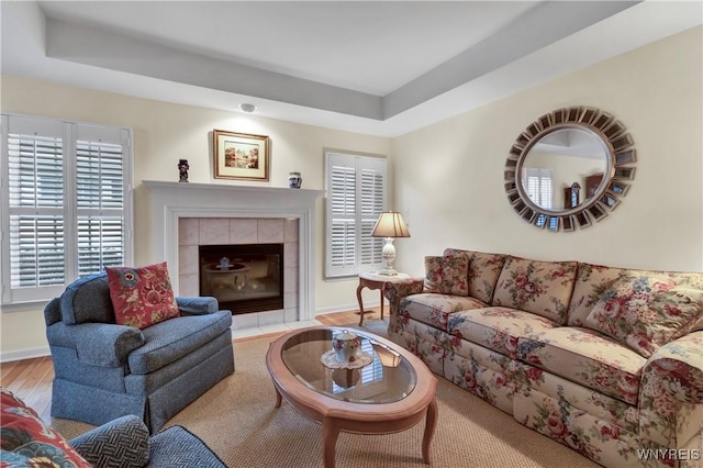 living area with baseboards, wood finished floors, a tray ceiling, and a tile fireplace