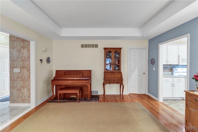 living area featuring a tray ceiling, light wood finished floors, and visible vents