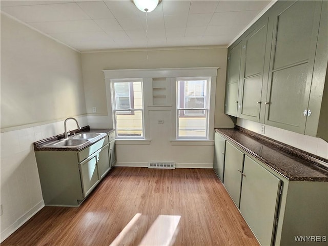 kitchen with dark countertops, a sink, light wood-style flooring, visible vents, and green cabinets