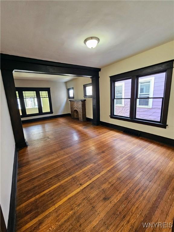unfurnished living room featuring baseboards, wood-type flooring, plenty of natural light, and a fireplace
