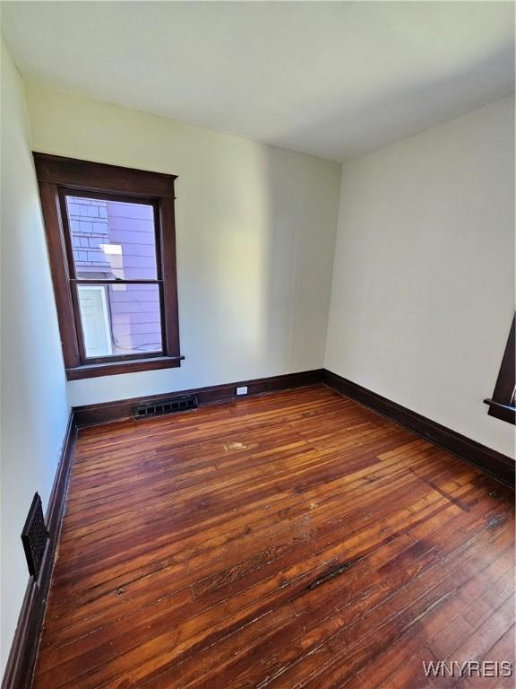 empty room featuring baseboards, dark wood finished floors, and visible vents