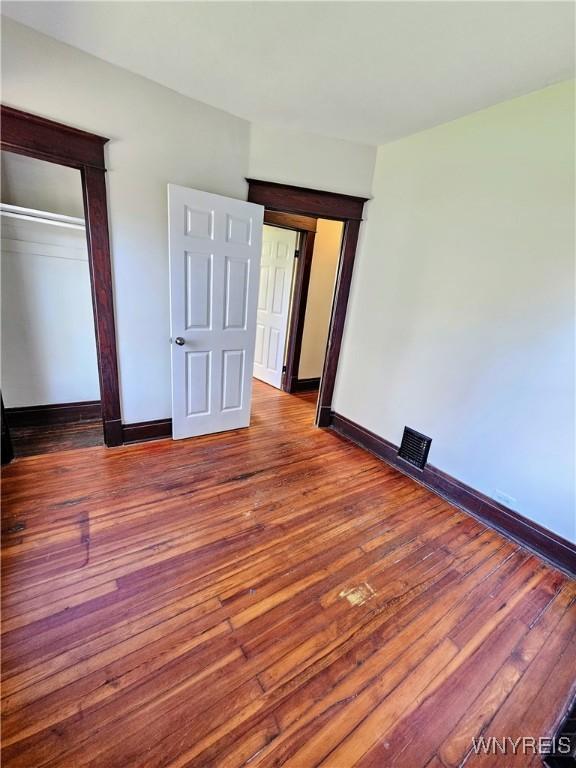 unfurnished bedroom featuring baseboards, visible vents, wood finished floors, and a closet
